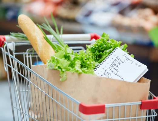 Grocery cart with a bag filled with lettuce, French bread, and a hand-written shopping list.