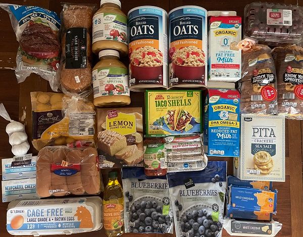 Aldi grocery haul displayed on a table. Including eggs, bread, milk, and more.